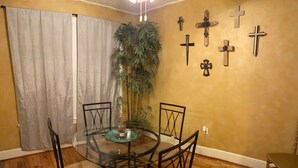 A dining area with a glass table, four chairs, a potted plant, and multiple crosses on the wall. - Cozy Downtown Home (Bryan)