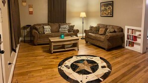 A living room with two sofas, a coffee table, a floor lamp, a ceiling fan, a rug, and a bookshelf. - Cozy Downtown Home (Bryan)