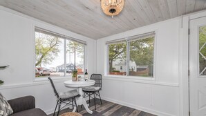 Una habitación con techo blanco, ventanas amplias, una mesa de comedor con sillas y un sofá gris.
