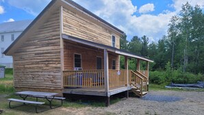 A wooden cabin with a porch, a picnic table, and a gravel driveway.