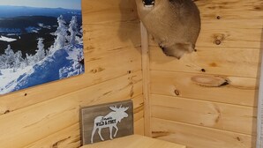 A wooden cabin interior with a mounted deer head on the wall, a framed picture of a snowy landscape, and a sign with a moose silhouette.