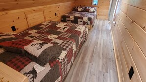 A cabin with two wooden beds, each with a quilted blanket.