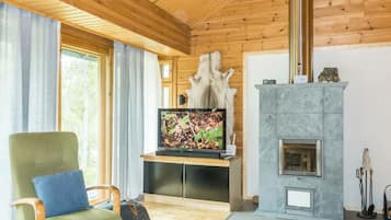 Tunnelmallinen olohuone, jossa on puinen katto, kivinen takka, televisio ja mukava nojatuoli.
