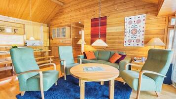 A cozy cabin interior with a wooden ceiling, a round wooden coffee table, and a blue rug.