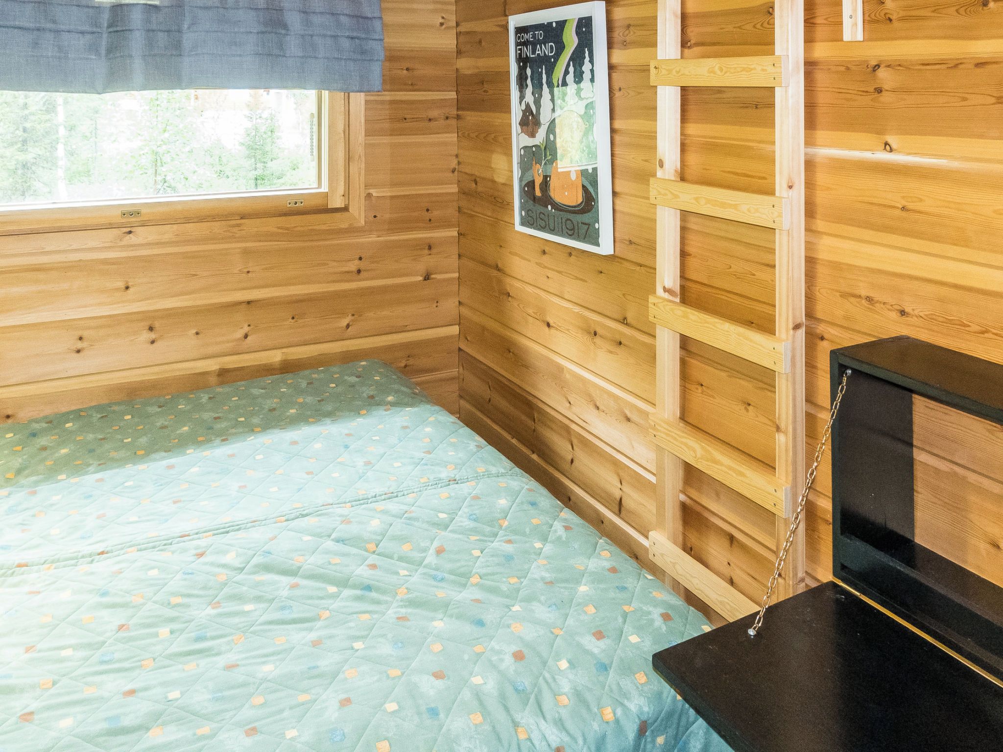 A wooden cabin room with a bed, a window, and a poster on the wall.