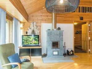 A wooden interior with a stone fireplace, a television on a wooden stand, and a chair with a cushion.
