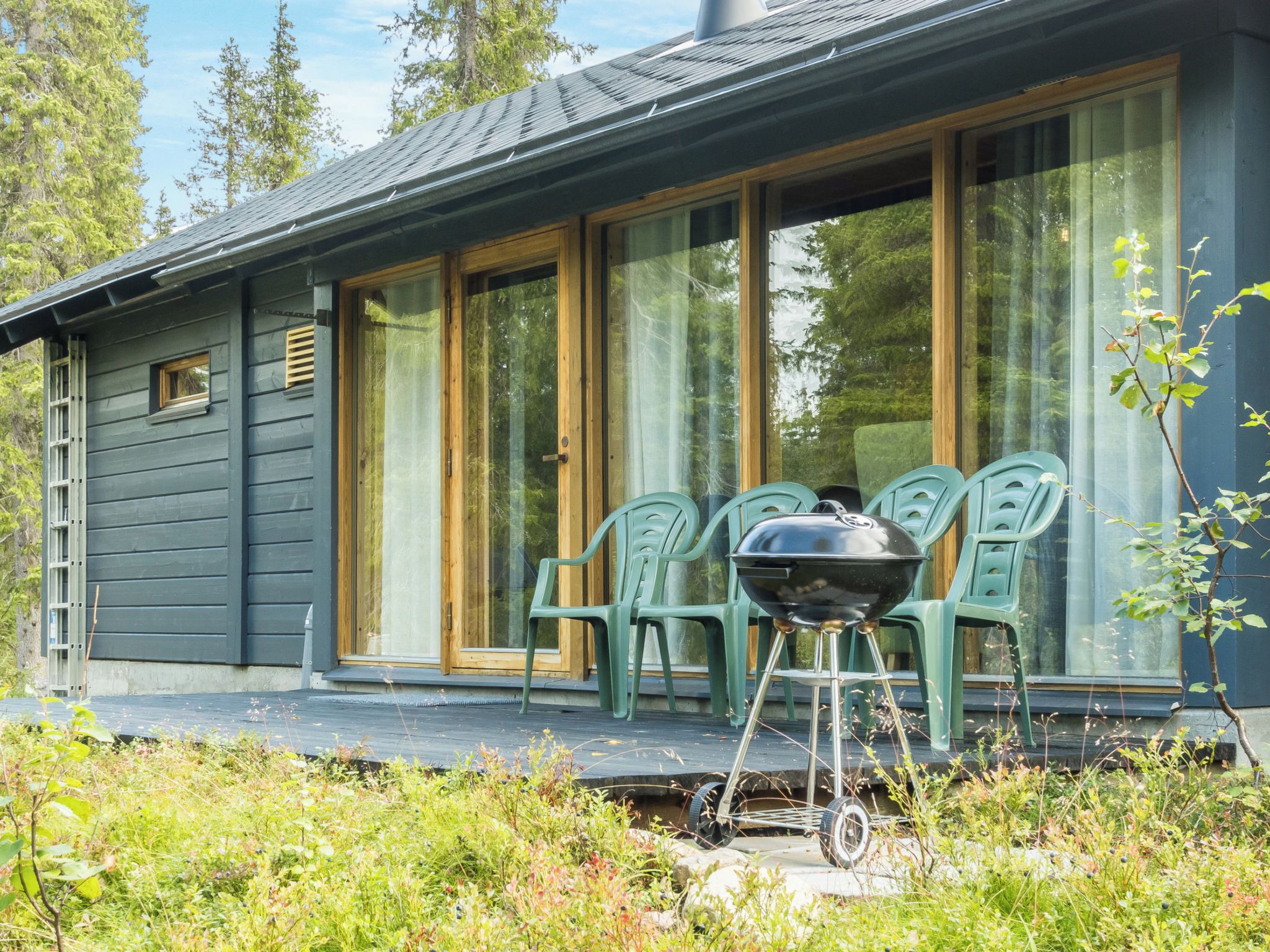 Ein Haus mit großen Glasschiebetüren, einer Veranda mit grünen Plastikstühlen und einem Grill.