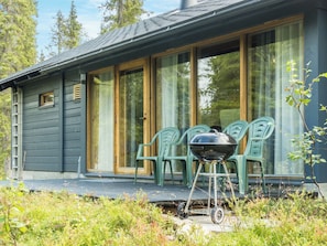A house with large sliding glass doors, a porch with green plastic chairs, and a barbecue grill. - Sinikuono by Interhome (Ylläsjärvi)