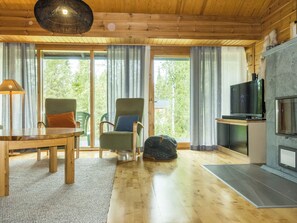 Una sala de estar acogedora con techo de madera, una mesa, dos sillas, un televisor y una chimenea.
