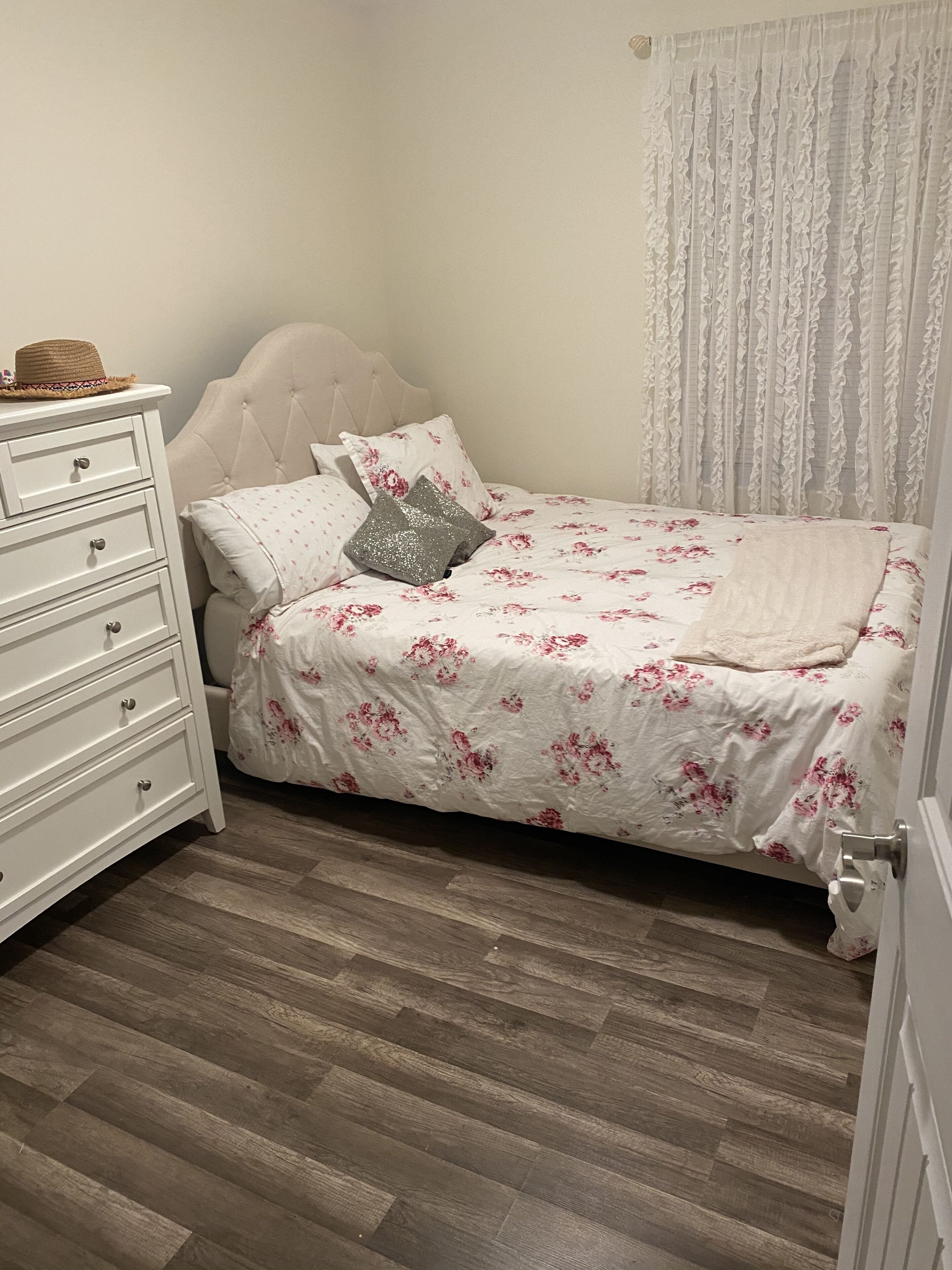 A bedroom with a bed, a dresser, and a window with curtains.