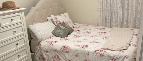 A bedroom with a bed, a dresser, and a window with curtains.