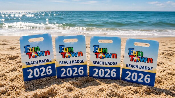 Quatre badges de plage avec les inscriptions « Fun Town » et « 2026 », sur une plage de sable, avec l’océan en arrière-plan.