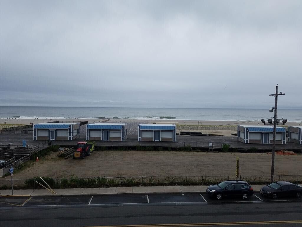 A beachside parking lot with several buildings, a tractor, and cars.
