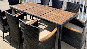 Une terrasse sur le toit, avec une table en bois et des chaises en osier, offrant une vue sur un quartier résidentiel avec des maisons et un château d’eau.