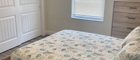 Un dormitorio con una cama de madera, una ventana con persianas, una puerta blanca y un aparador de madera.