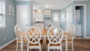 A dining area with a wooden table and white chairs, a kitchen with white appliances, and light blue walls. - Prime Location Close to the Beach and Boardwalk (Ocean City)