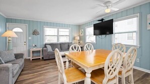 A dining area with a wooden table and white chairs, a gray sofa, and a ceiling fan. - Prime Location Close to the Beach and Boardwalk (Ocean City)