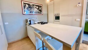 Een kleine keuken met een wit aanrecht, een gasfornuis, een magnetron en een kunstwerk in een lijst aan de muur.