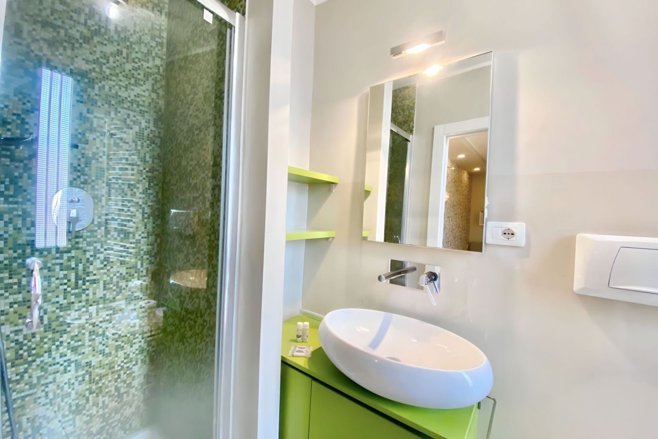 Une salle de bain moderne avec une douche à parois de verre, un lavabo blanc et un meuble-lavabo vert.