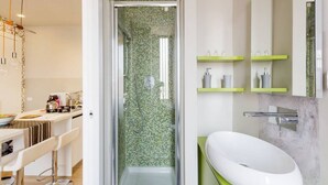 Een moderne badkamer met een douche, een witte wastafel en groene schappen.