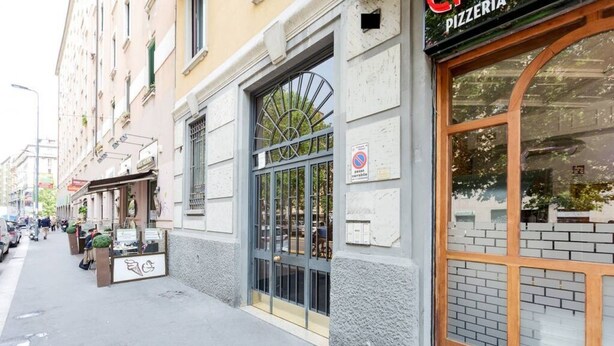 Straatbeeld met een pizzeria aan de rechterkant, een trottoir en een gebouw met een traliesraam.