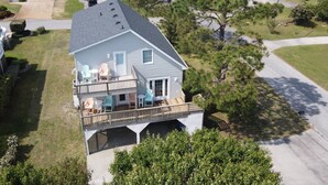 A two-story house with a balcony, a covered deck, and a small front yard. - Island Haven - Hot Tub & Beautiful Water Views (Nags Head)
