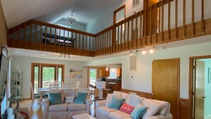 A spacious living area with a high ceiling, a balcony, and a kitchen in the background. - Island Haven - Hot Tub & Beautiful Water Views (Nags Head)