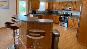 A modern kitchen with wooden cabinets, stainless steel appliances, and a bar area with stools. - Island Haven - Hot Tub & Beautiful Water Views (Nags Head)