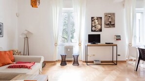 A living room with a sofa, a coffee table, a TV on a stand, and a window with curtains. - Washington Cosy and Comfortable Apartment (Milano)