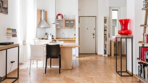 A modern kitchen with a dining area, a bookshelf, and a red vase on a table. - Washington Cosy and Comfortable Apartment (Milano)