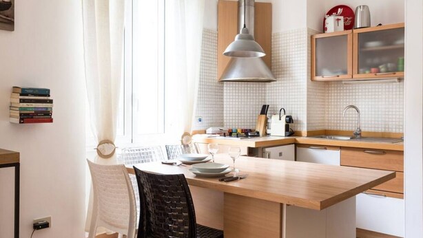 A kitchen with a wooden island, a hanging pendant light, a window with curtains, and a countertop with kitchenware. - Washington Cosy and Comfortable Apartment (Milano)