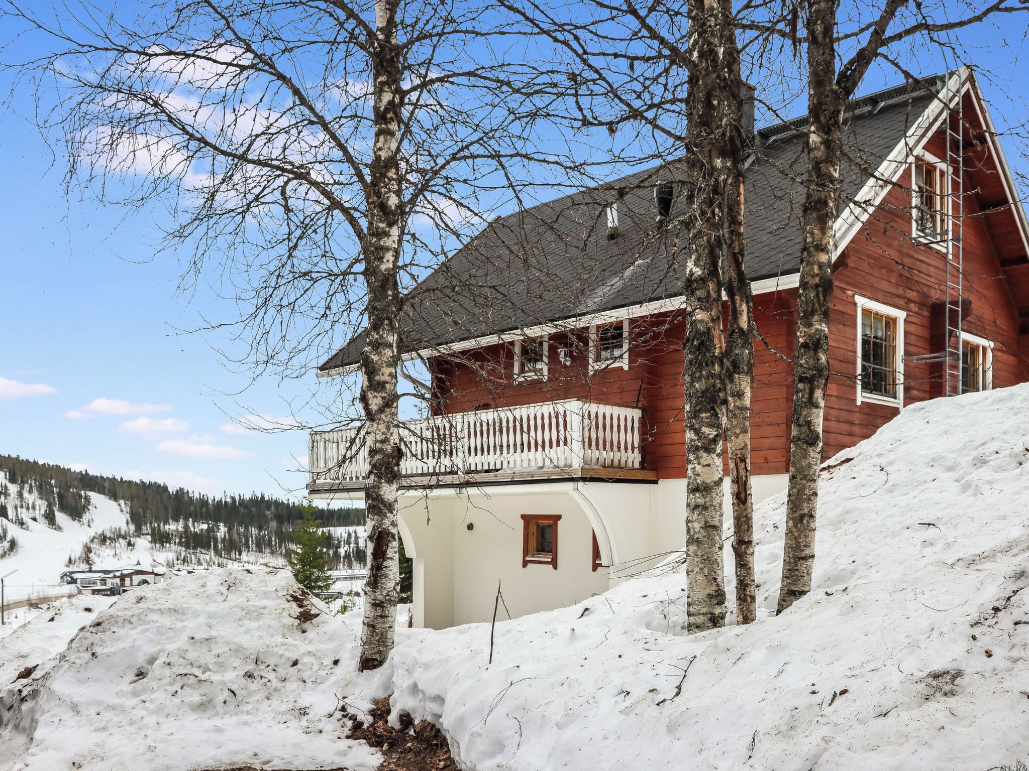 Una casa de madera con balcón, rodeada de nieve y árboles.