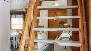 Una escalera de madera conduce a una zona de cocina con armarios blancos y un comedor con sillas blancas.