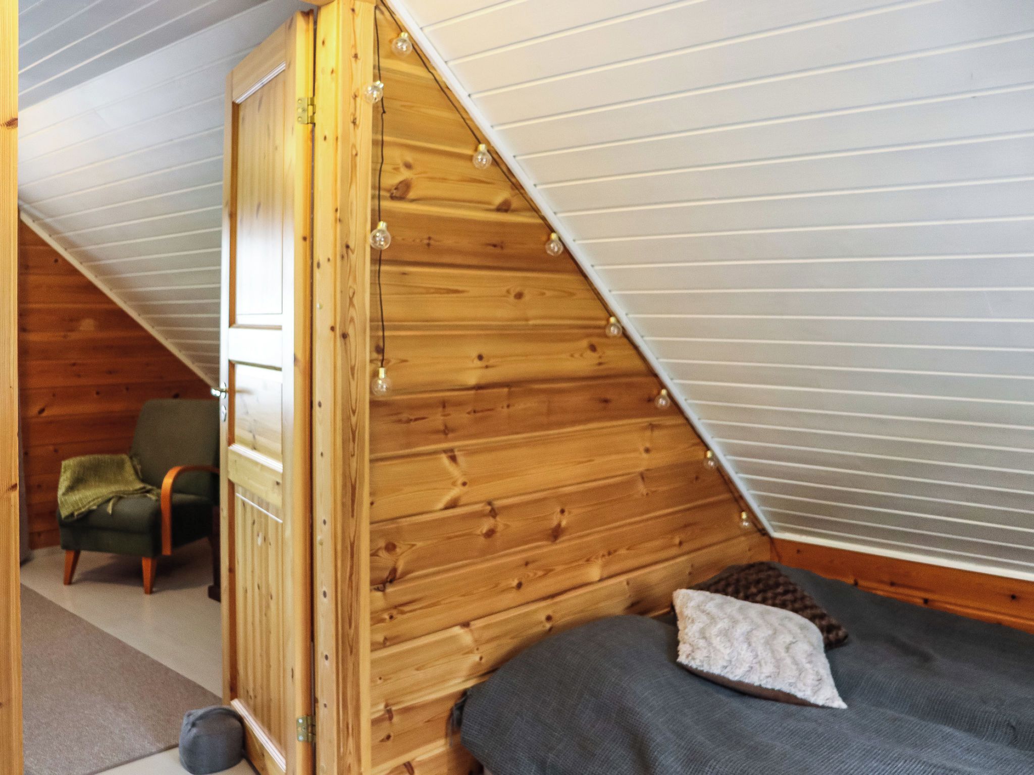 A small, cozy room with a sloped ceiling, a wooden door, a single bed, and a chair.