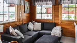 Una habitación acogedora con un sofá seccional gris oscuro, un reposapiés a juego y suelo de madera. Hay dos ventanas con cortinas grises, y un cuadro cuelga en la pared.