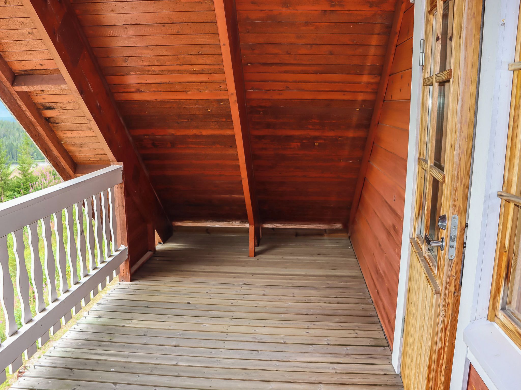 Un balcon en bois avec une balustrade blanche, un plancher en bois et une fenêtre dotée d’une poignée en métal.