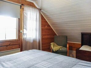 A bedroom with a bed, a chair, and a window with curtains.
