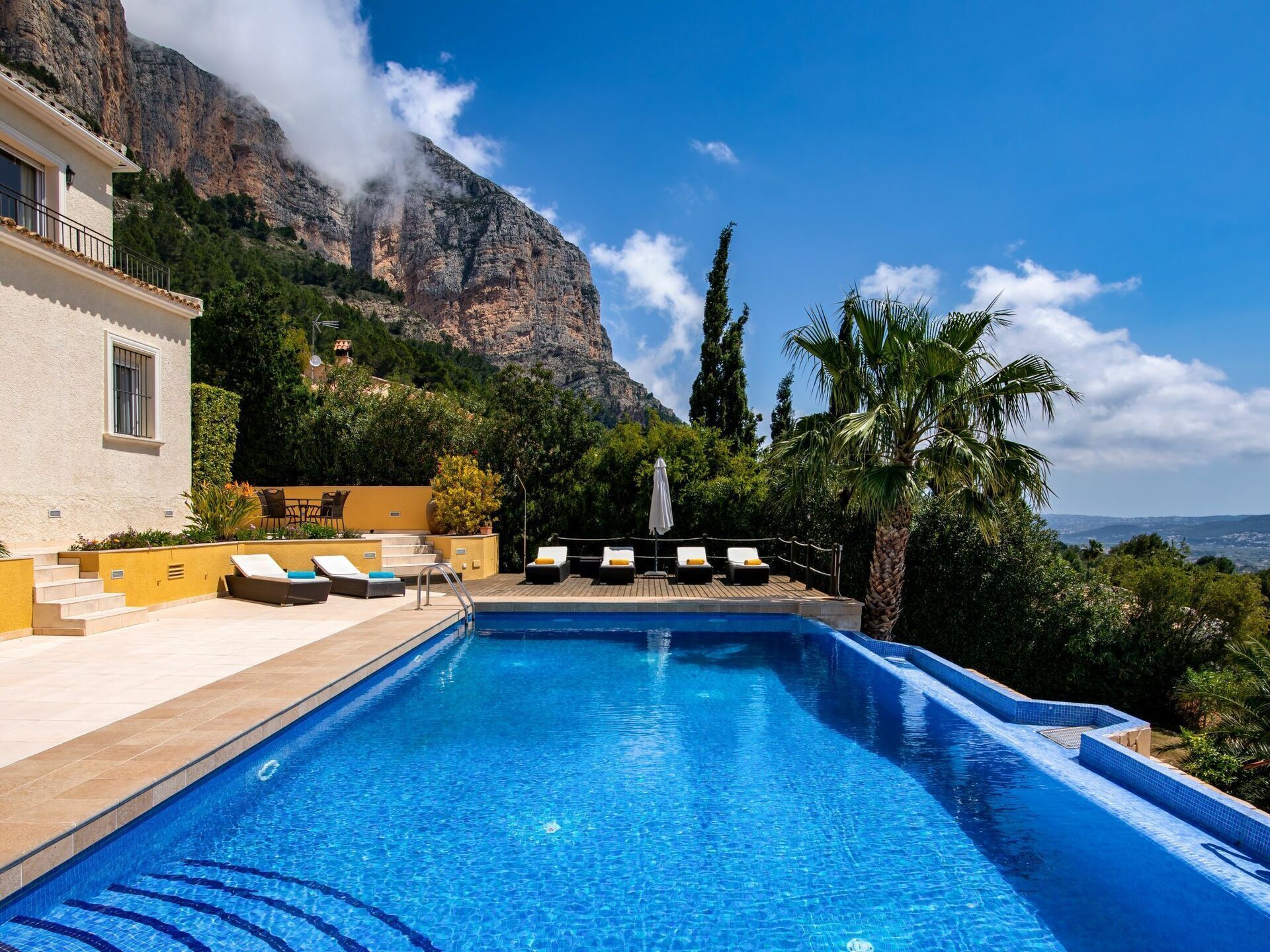 Piscina com espreguiçadeiras e montanhas ao fundo.