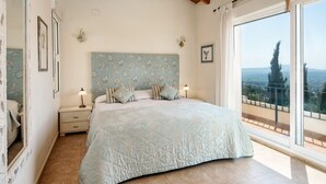 Camera da letto con un letto grande, un comodino, una cassettiera e vista sulla città da un balcone.