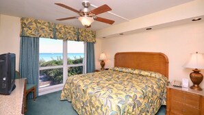 Habitación de hotel con cama, ventilador de techo, televisor, escritorio y ventana con vistas.