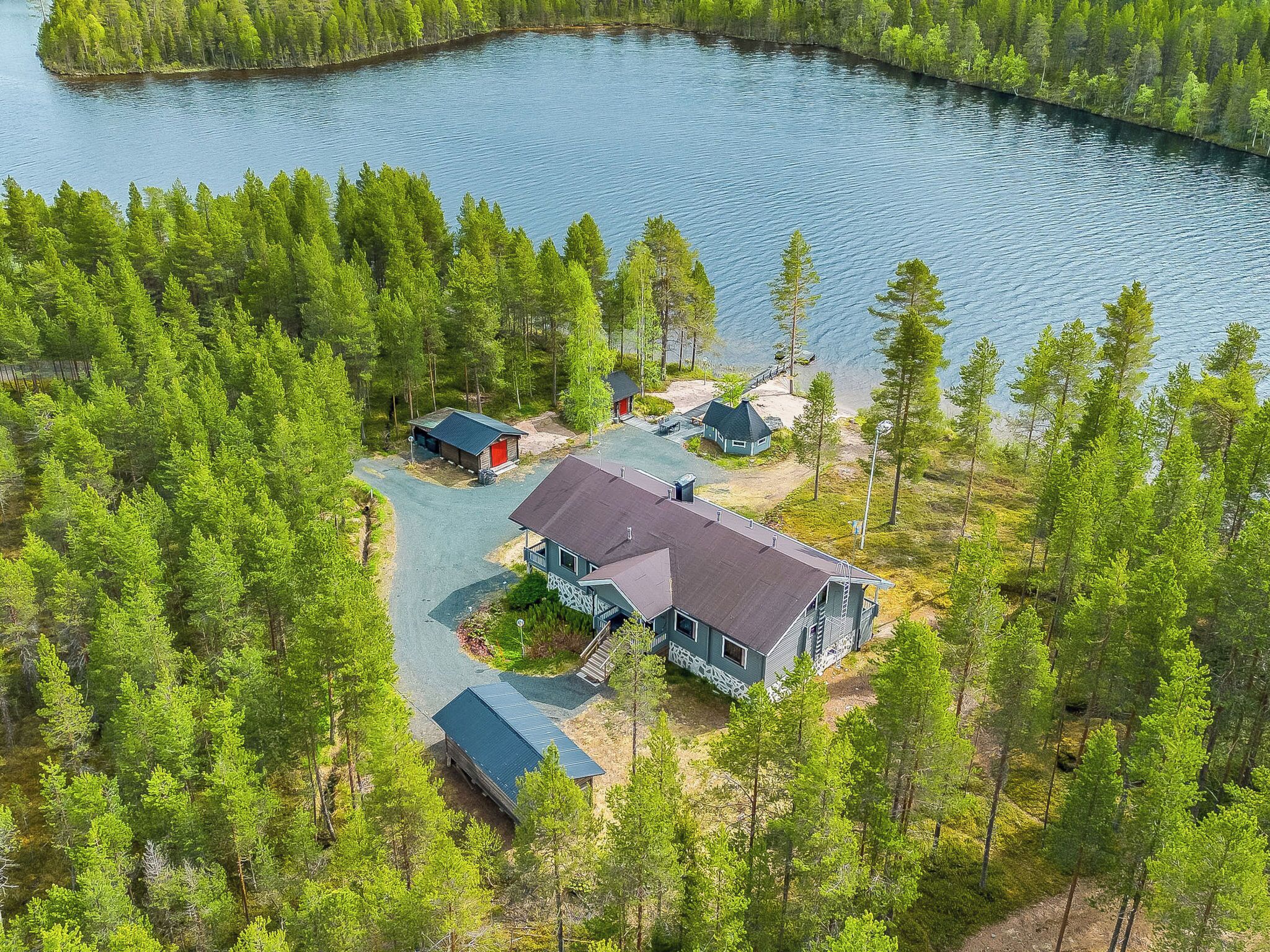 Eine Blockhütte am Seeufer mit einer großen Terrasse, umgeben von dichtem Wald.