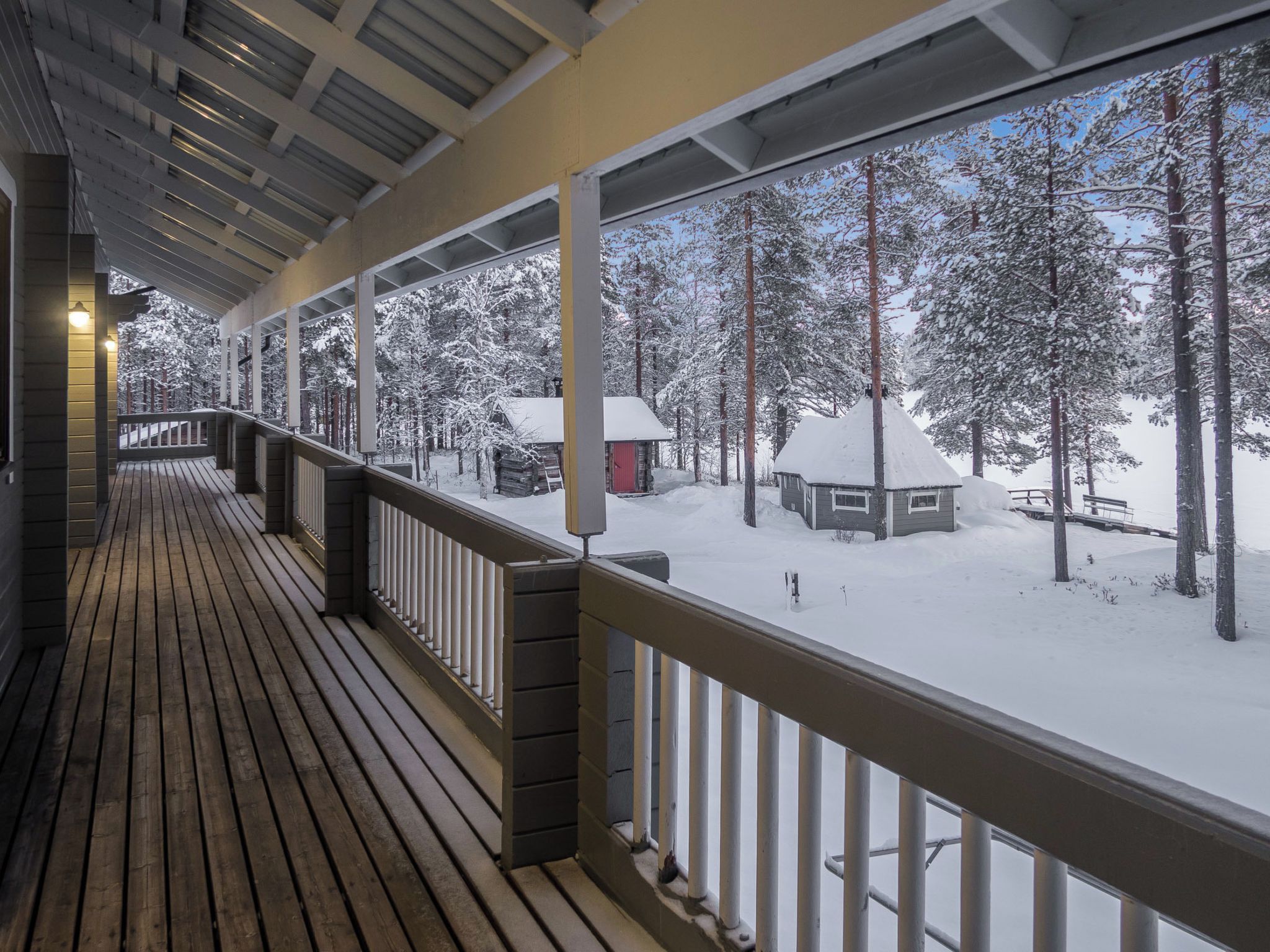 Une terrasse en bois couverte, dotée d’une rambarde, qui offre une vue sur un paysage enneigé, avec des arbres et un chalet.