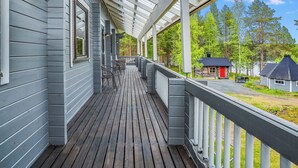 A covered porch with a wooden deck, outdoor seating, and a view of a forested area.