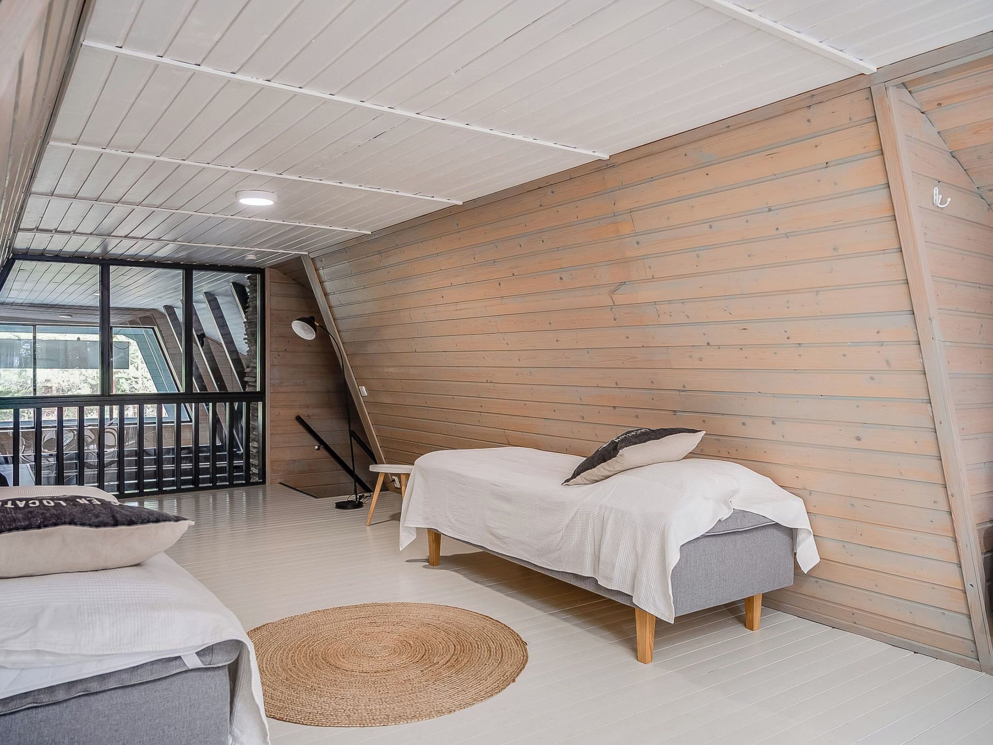 Una camera da letto con un letto, un tavolino, una sedia, un tappeto tessuto e vista sull'esterno attraverso una finestra.