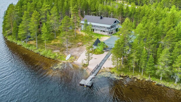 A lakeside cabin surrounded by dense forest, with a dock extending into the water.