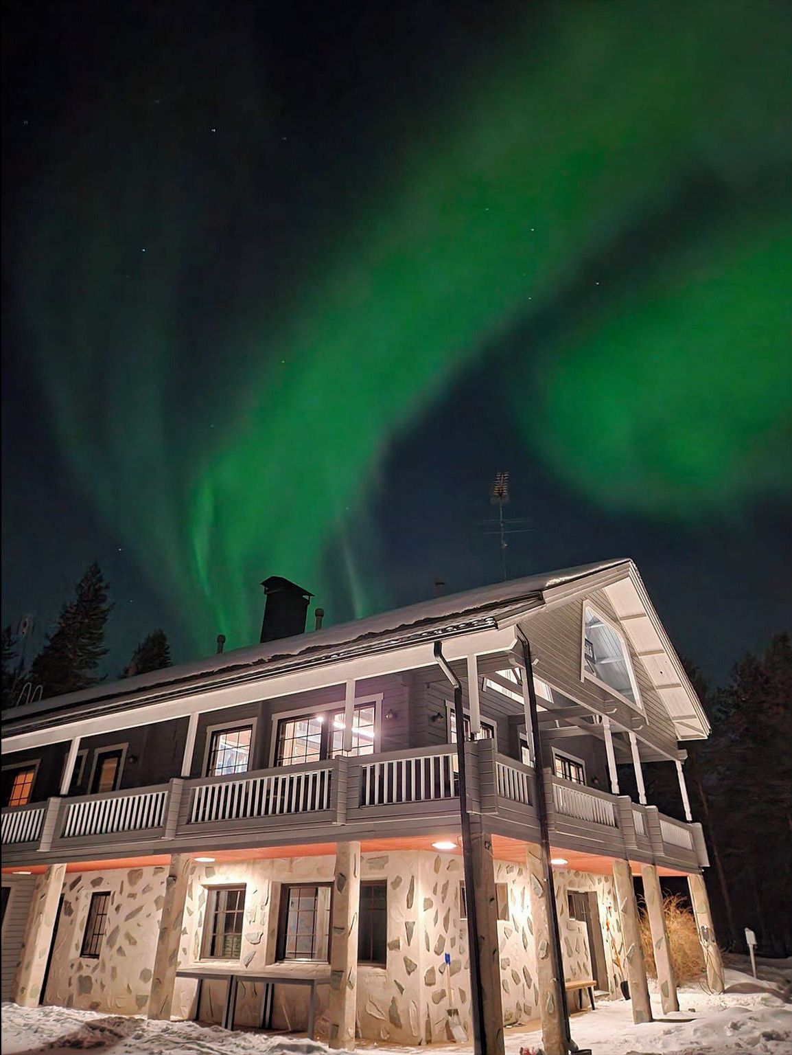 A two-story building with a stone facade and a balcony, under a night sky with green aurora borealis.