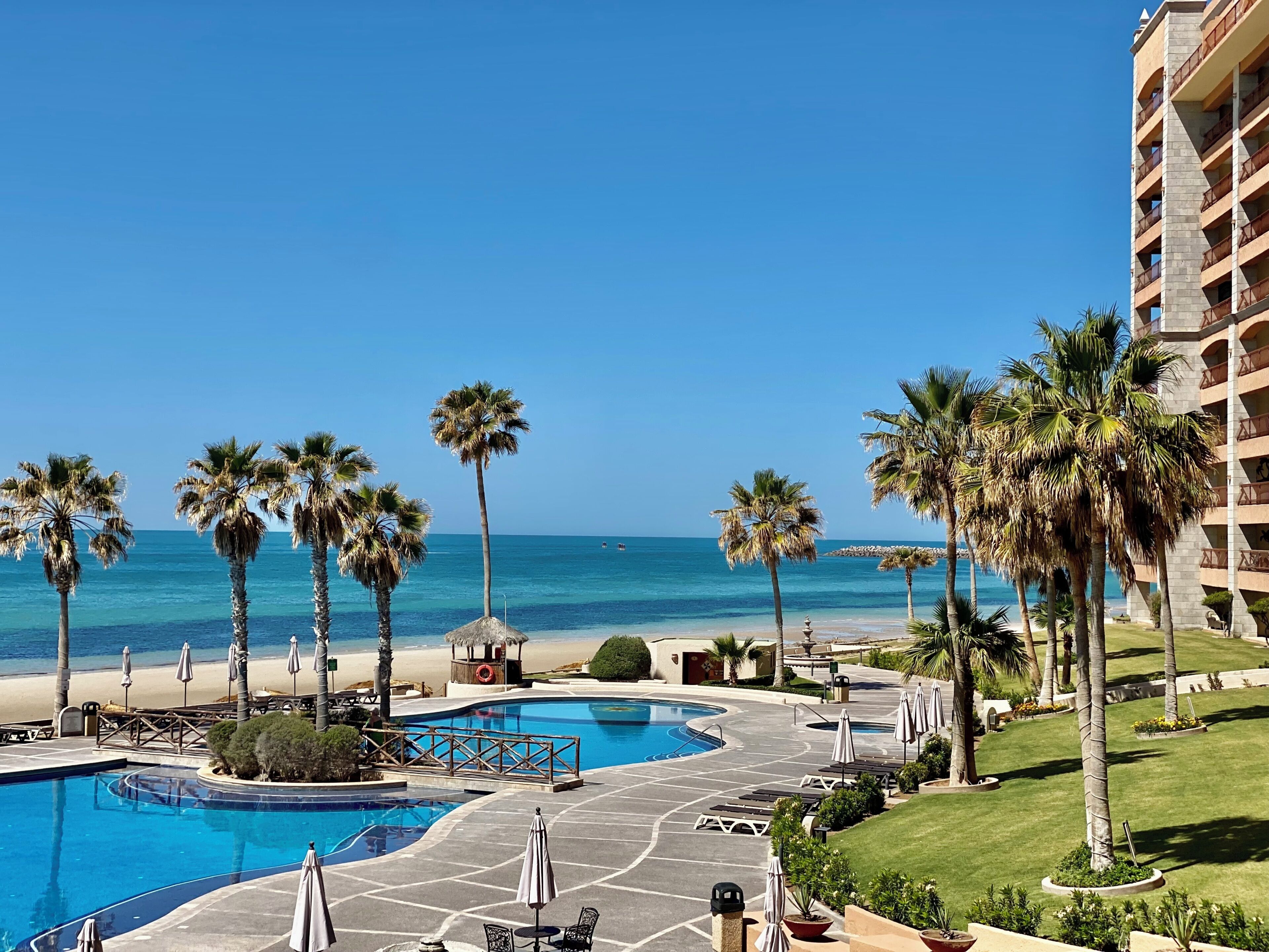 A resort pool area with a view of the beach and ocean.