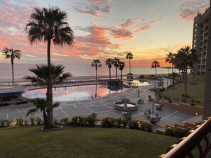 A resort pool area with palm trees, a circular water feature, and a view of the ocean at sunset. - 🌴MODERN 1 BEDROOM OCEANFRONT CONDO WITH BREATHTAKING VIEWS SONORAN SUN RESORT🌴 (Puerto Peñasco)