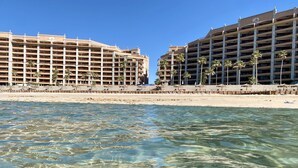 Een strandhotel met meerdere verdiepingen, palmbomen en een zandstrand.