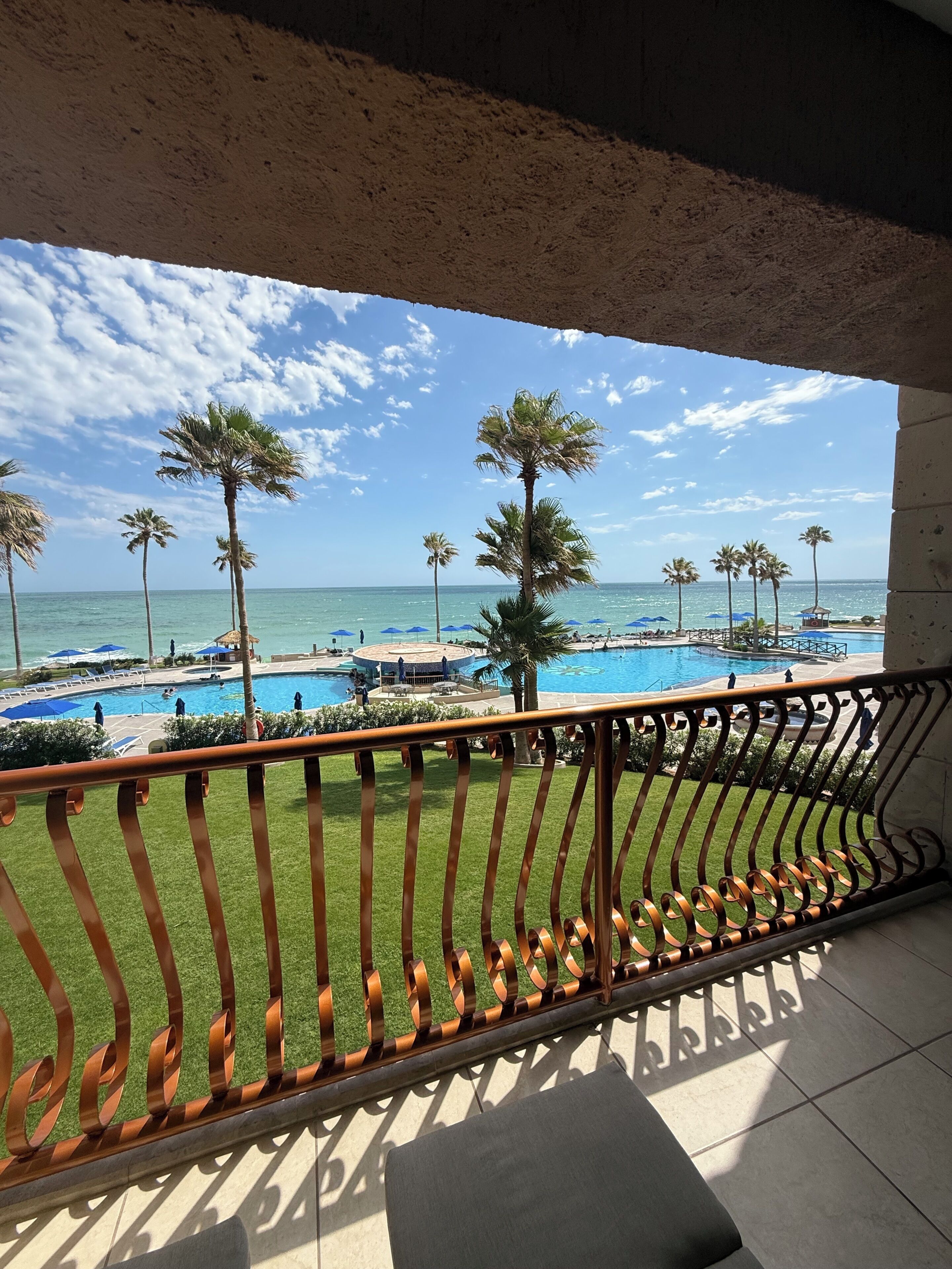 Een balkon met uitzicht op een zwembad, palmbomen en de oceaan.
